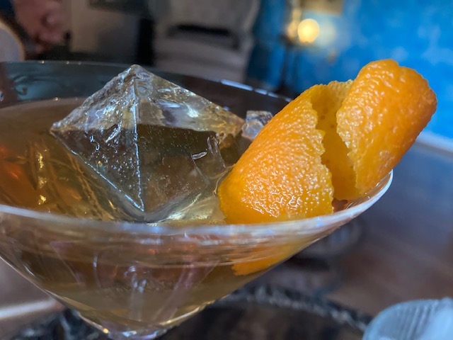 Perfect Manhattan: Light brown cocktail over large cube garnished with curled orange peel