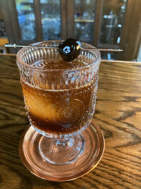 Tootsie Roll: Brown drink in a stemmed old-fashioned glass, with a speared Luxardo cherry.