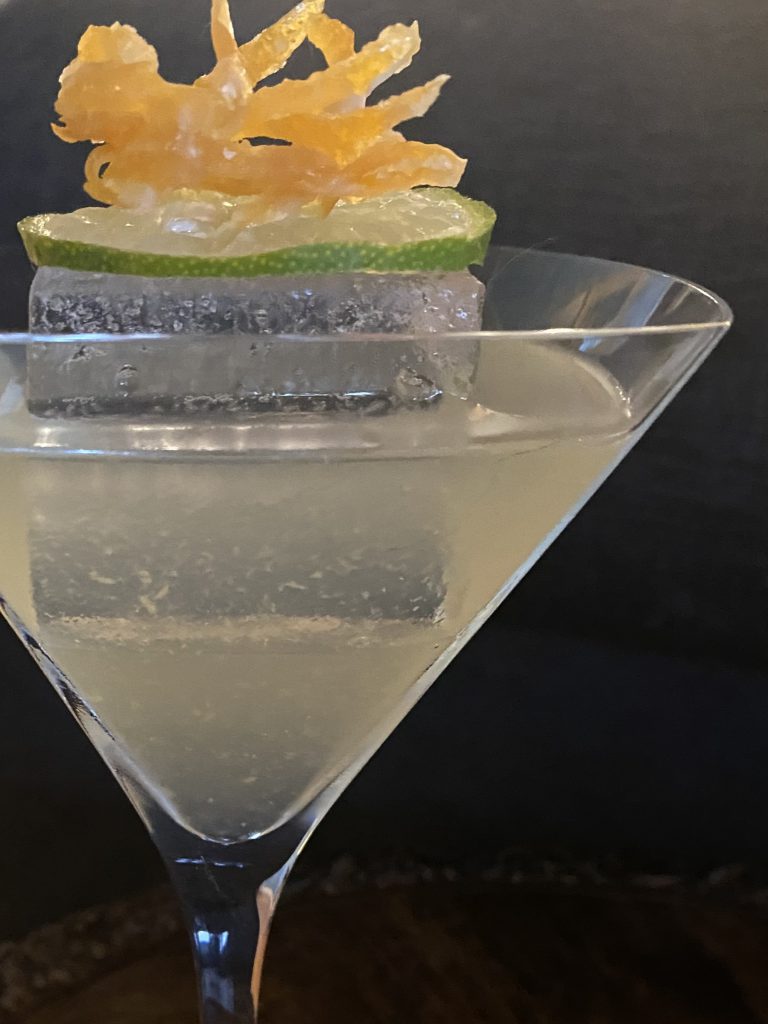Basil Daiquiri: Cloudy drink with a large, clear ice cube, decorated with a lime wheel and candied ginger