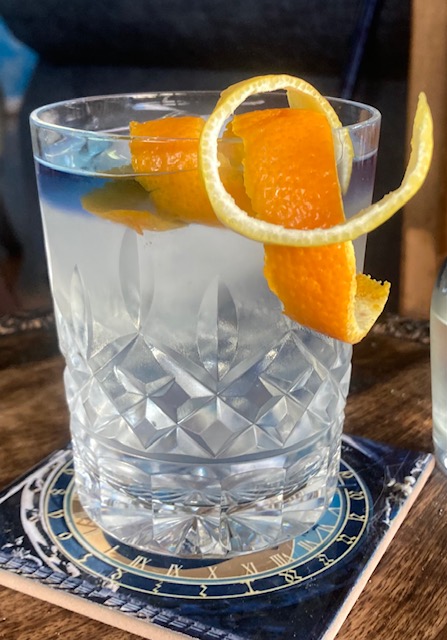 Citrus Gimlet with Butterfly Pea Flower Float: Clear cocktail in an old-fashioned glass with lemon and orange peel curls and a blue float