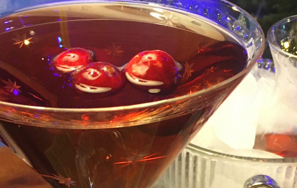 Holiday Cranberry Manhattan: Brown cocktail in a martini glass with three cranberries