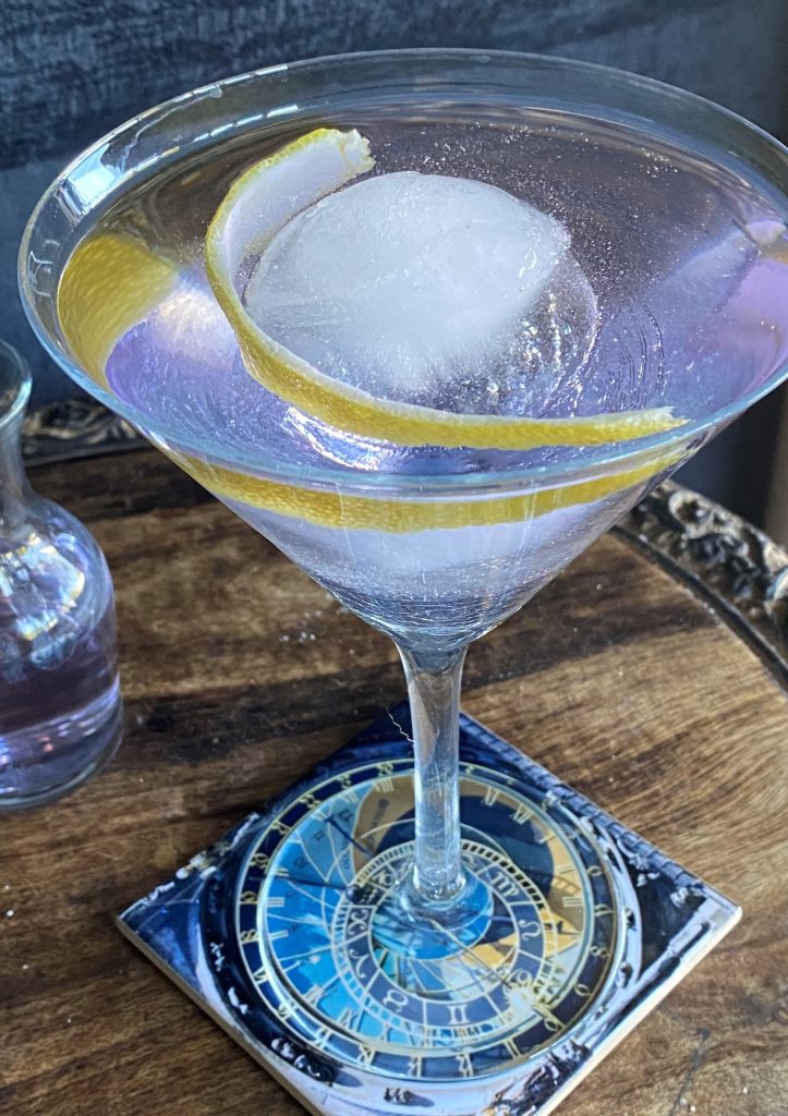 Martini Twist: Clear cocktail in a martini glass with a large ice cube and lemon peel garnish