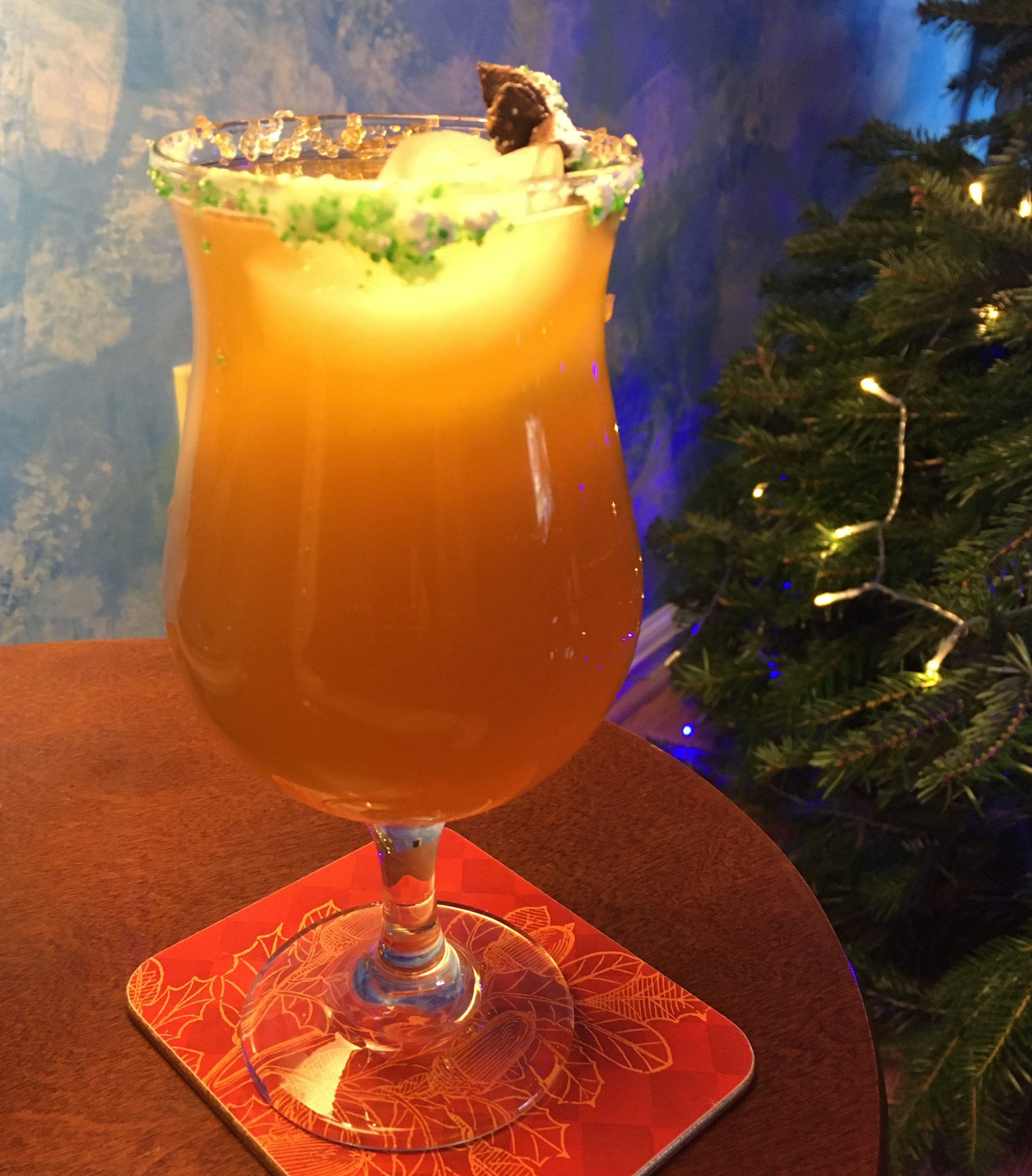 Star Anise Vanilla Rum Dram: Amber drink in a hurricane glass with green and gold sugar and star anise