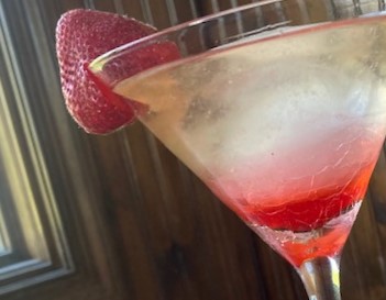 Strawberry Gimlet: Clear cocktail with muddled strawberries and a large ice sphere in martini glass with whole strawberry garnish