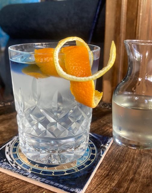 Citrus Gimlet with Butterfly Pea Flower Float: Clear cocktail in an old-fashioned glass with lemon and orange peel curls and a blue float
