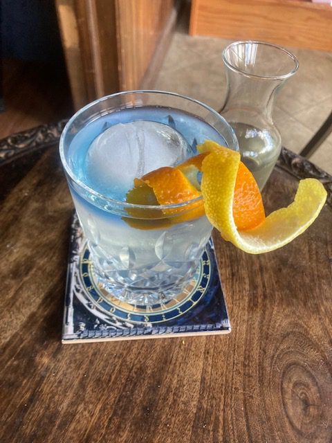 Citrus Gimlet with Butterfly Pea Flower Float: Clear cocktail in an old-fashioned glass with lemon and orange peel curls and a blue float