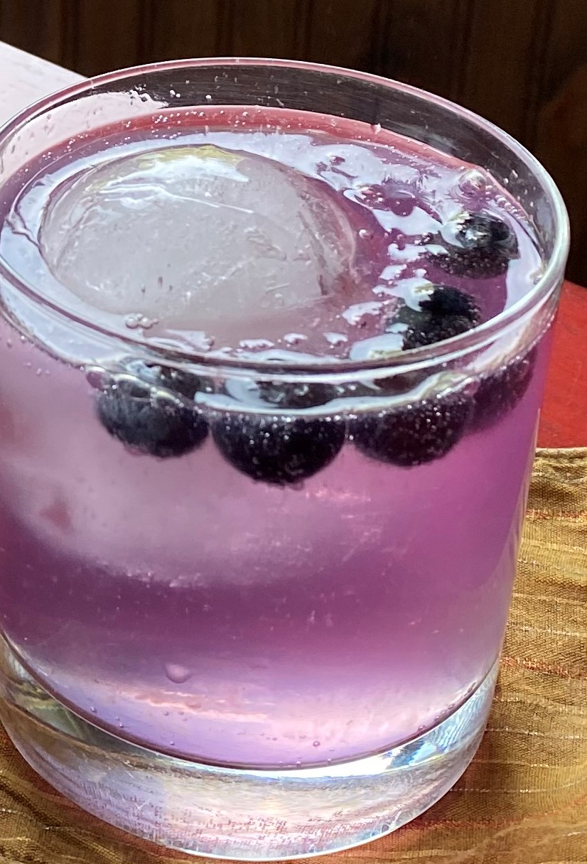Empress Collins Blueberry: Purple cocktail in an old-fashioned glass garnished with blueberries