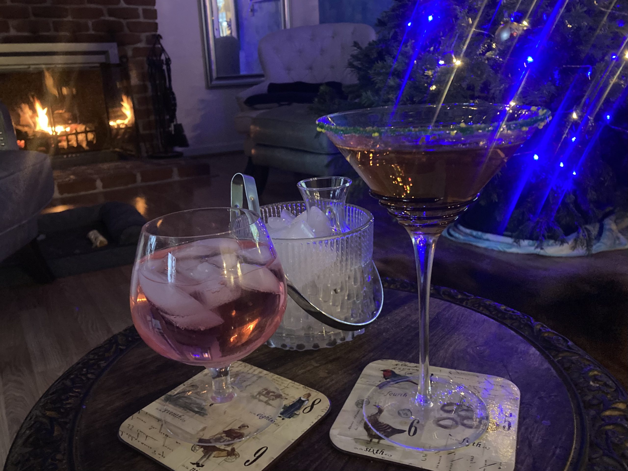 Pair of Fireplace Drinks: Blush iced cocktail in a goblet and a brown cocktail in a martini glass with a green sugar rim