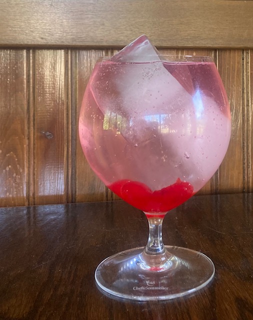 Smoked Cherry Gin and Tonic: Clear cocktail in a goblet with muddled maraschino cherries and two large ice cubes