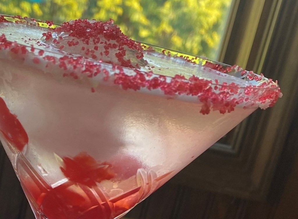 Cherry Gin and Tonic: Clear drink with maraschino cherries and an ice sphere in a martini glass, garnished with a red sugar rim.
