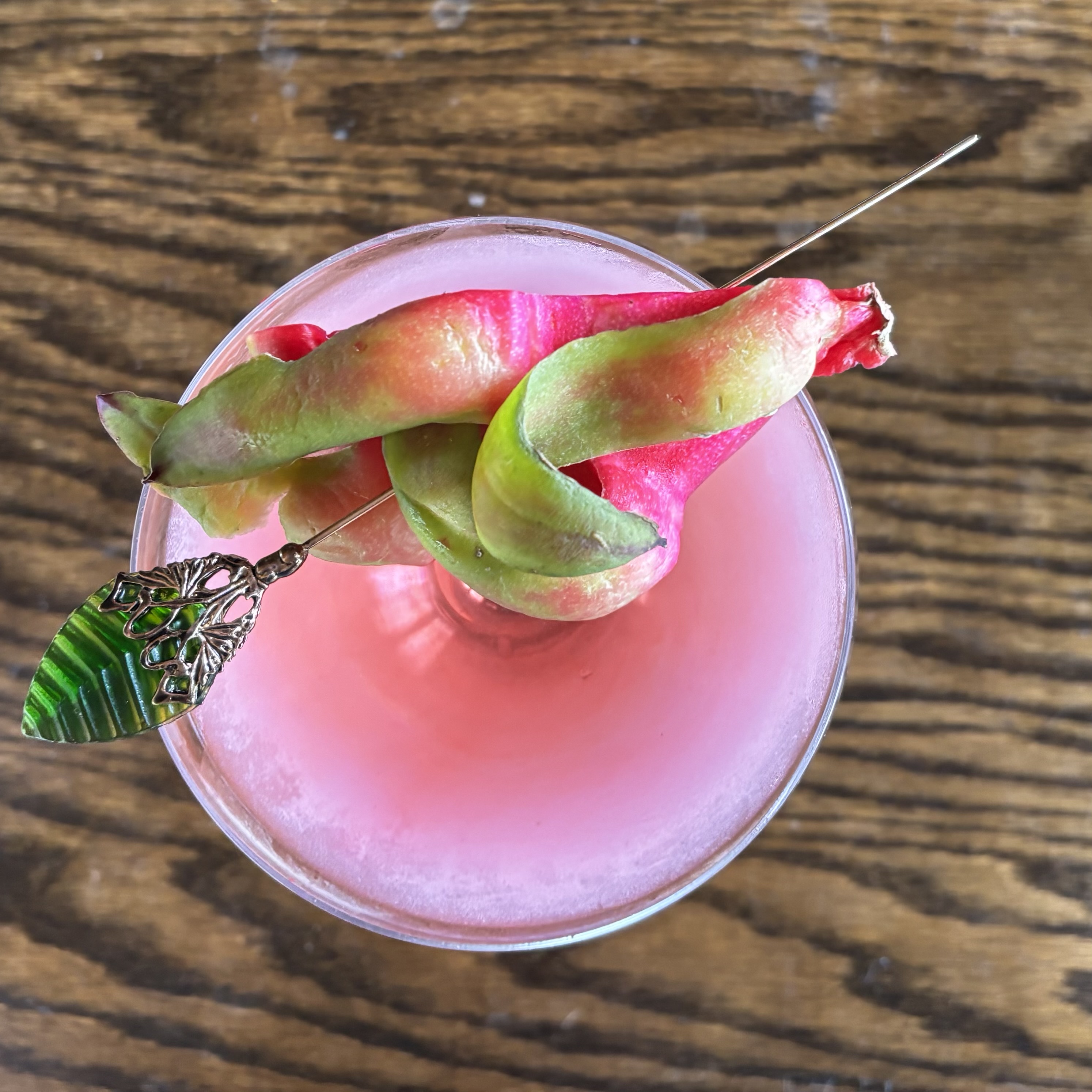 Pink Dragonfruit Garden: Foamy pink cocktail in a coupe garnished with a slice of dragonfruit on a hairpin.