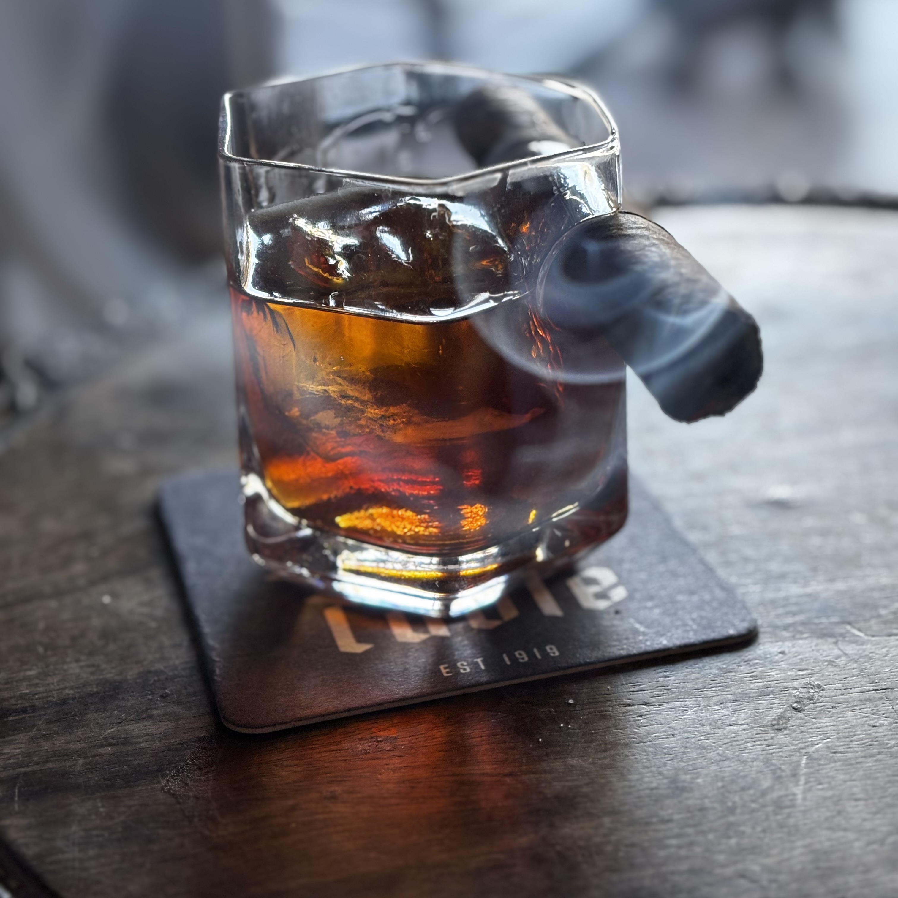 100 Year Old Cigar: Chestnut brown drink in short glass with a cigar holder garnished with a smoking cigar