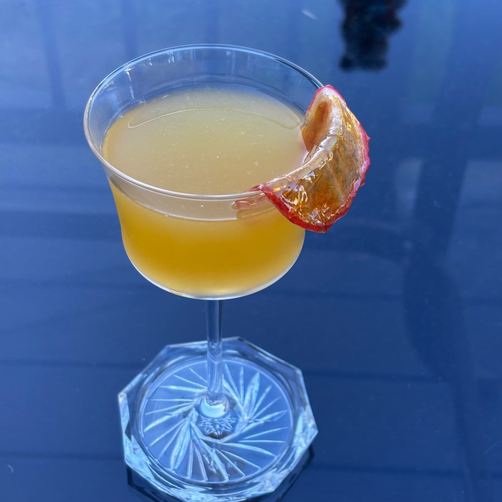 Picasso's Apple: Nick and Nora glass with golden drink garnished with a "melted" stained glass candied apple slice